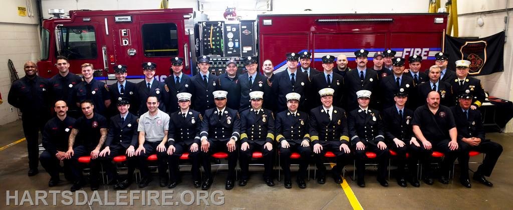 A group of firefighters posed in front of a fire truck inside a fire station, with "Hartsdale Fire" visible.