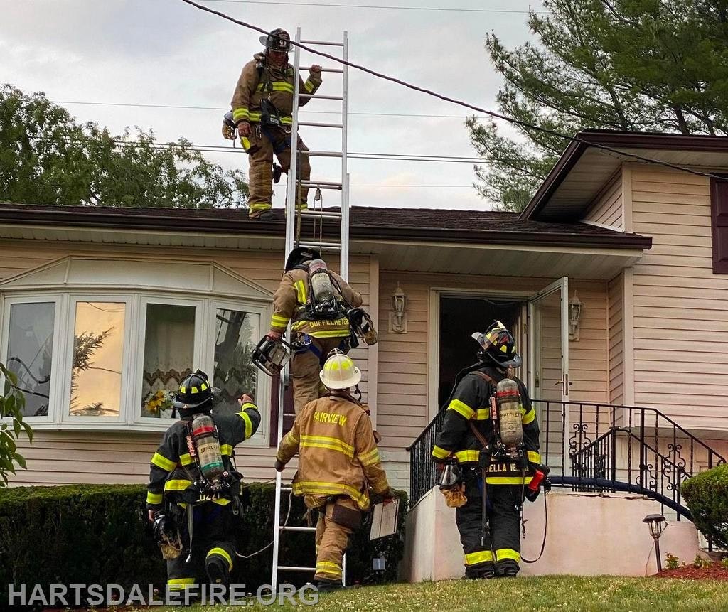 Firefighters in gear using a ladder to access a roof on a house.