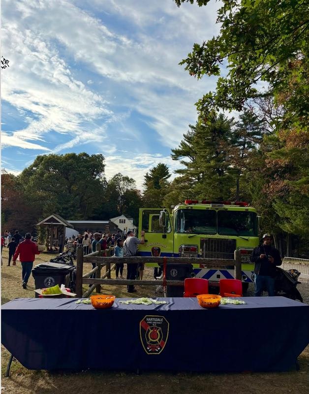 A busy outdoor event with a bright green fire truck, tables with bowls, and people enjoying the festivities under a clear sky.