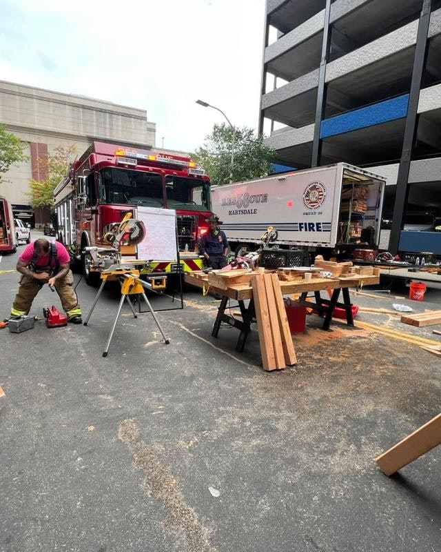 A fire truck and service vehicle are parked, with firefighters working on woodworking projects and tools set up nearby.