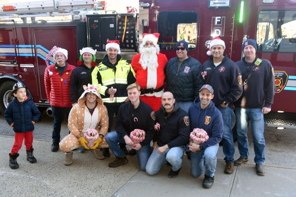 A group of people in festive attire, including Santa, posing with a fire truck.
