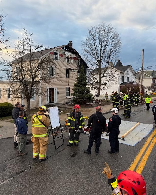 Emergency responders are at the scene of a damaged building, likely due to a fire or accident, with firefighters and personnel present.