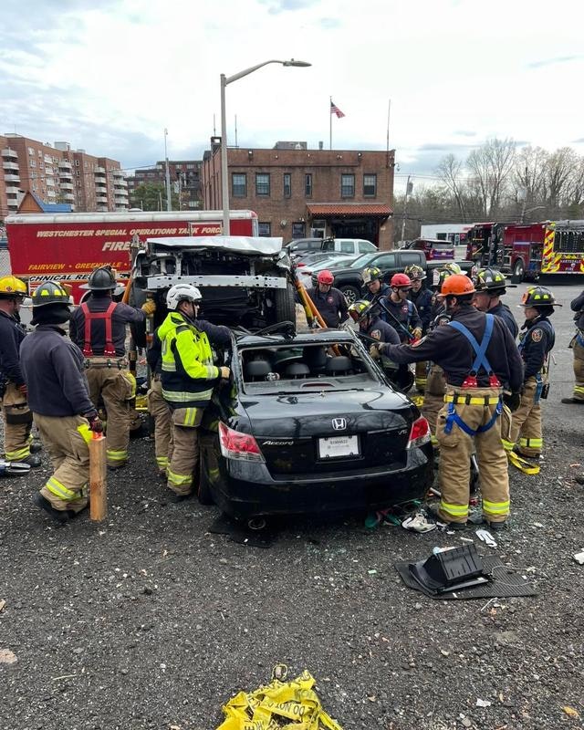 Firefighters and rescuers are working around a damaged car at an emergency scene, likely involving a crash or rescue operation.