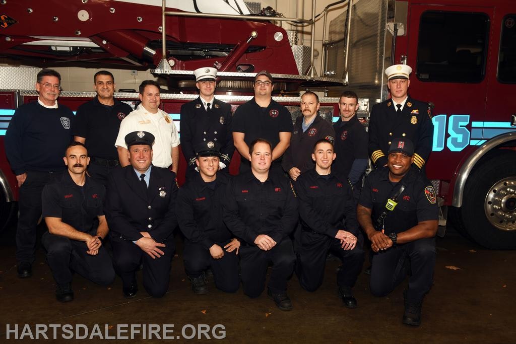 A group of firefighters poses together in front of a fire truck, showcasing their teamwork and dedication to service.