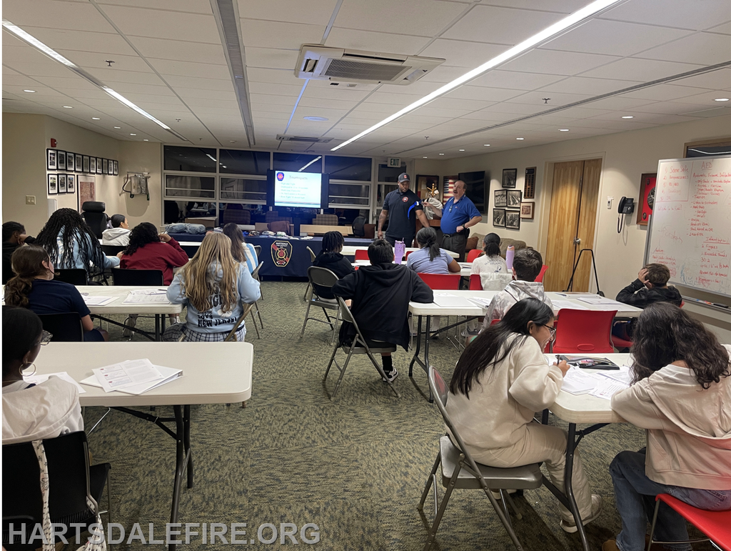 A classroom setting with students learning, while two instructors present information on a screen.