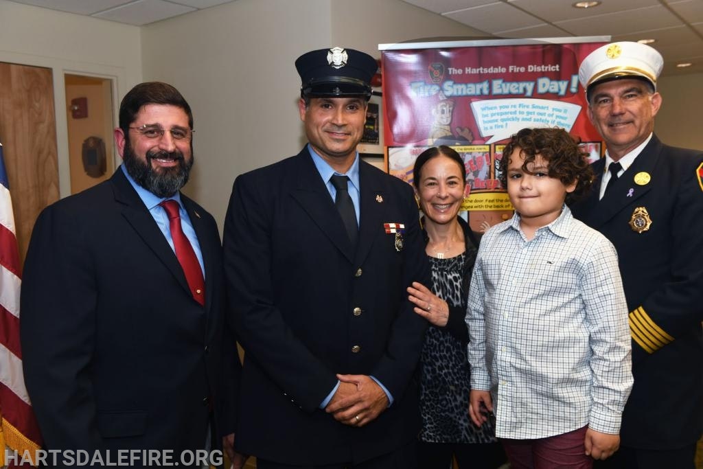 A group of people, including firefighters, posing indoors near a fire safety poster.