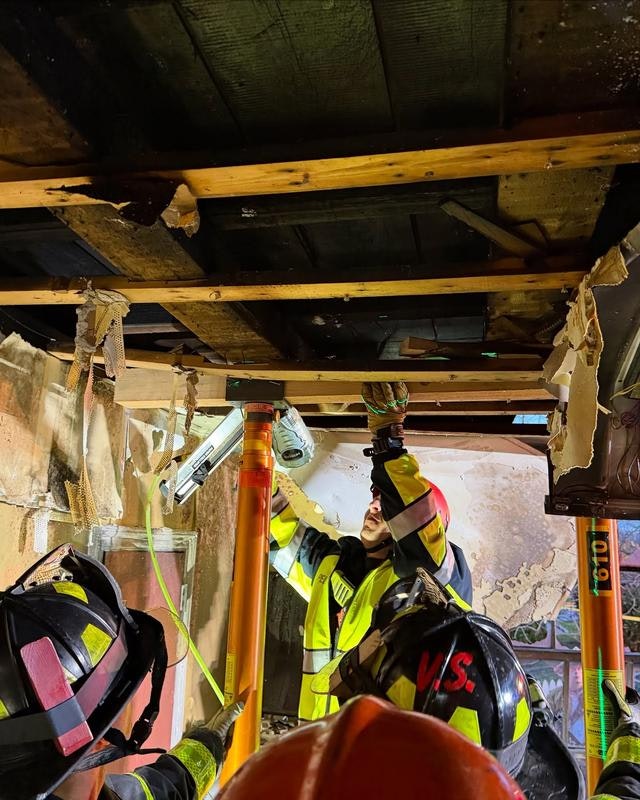 Firefighters are assessing and stabilizing a damaged structure using support poles and tools in a collapsed area.