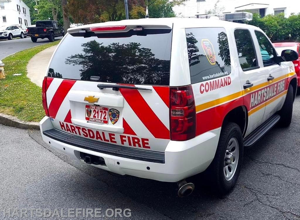A Hartsdale Fire Department command vehicle parked on the street with red and white chevron stripes.