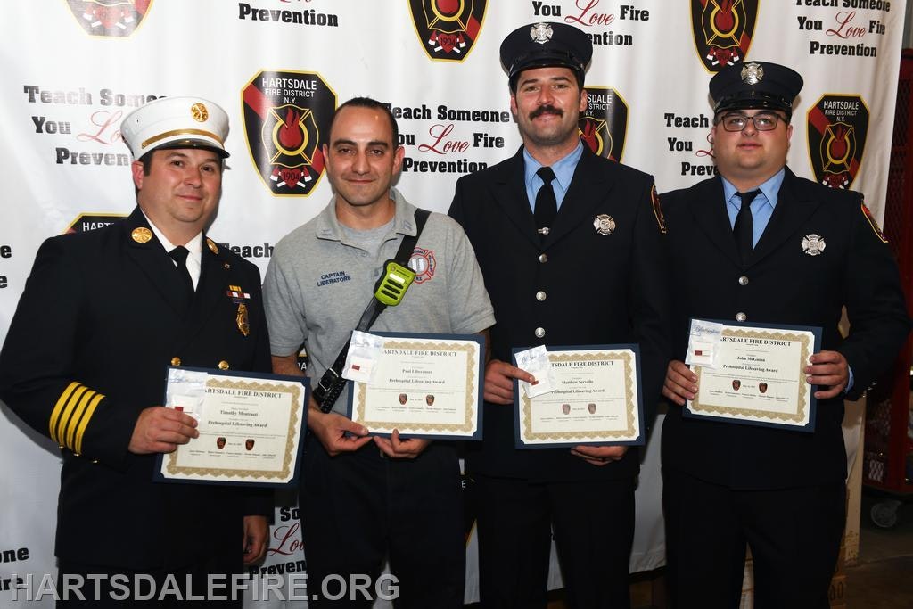 Four firefighters with awards at a recognition event, standing in front of a Hartsdale Fire District banner.
