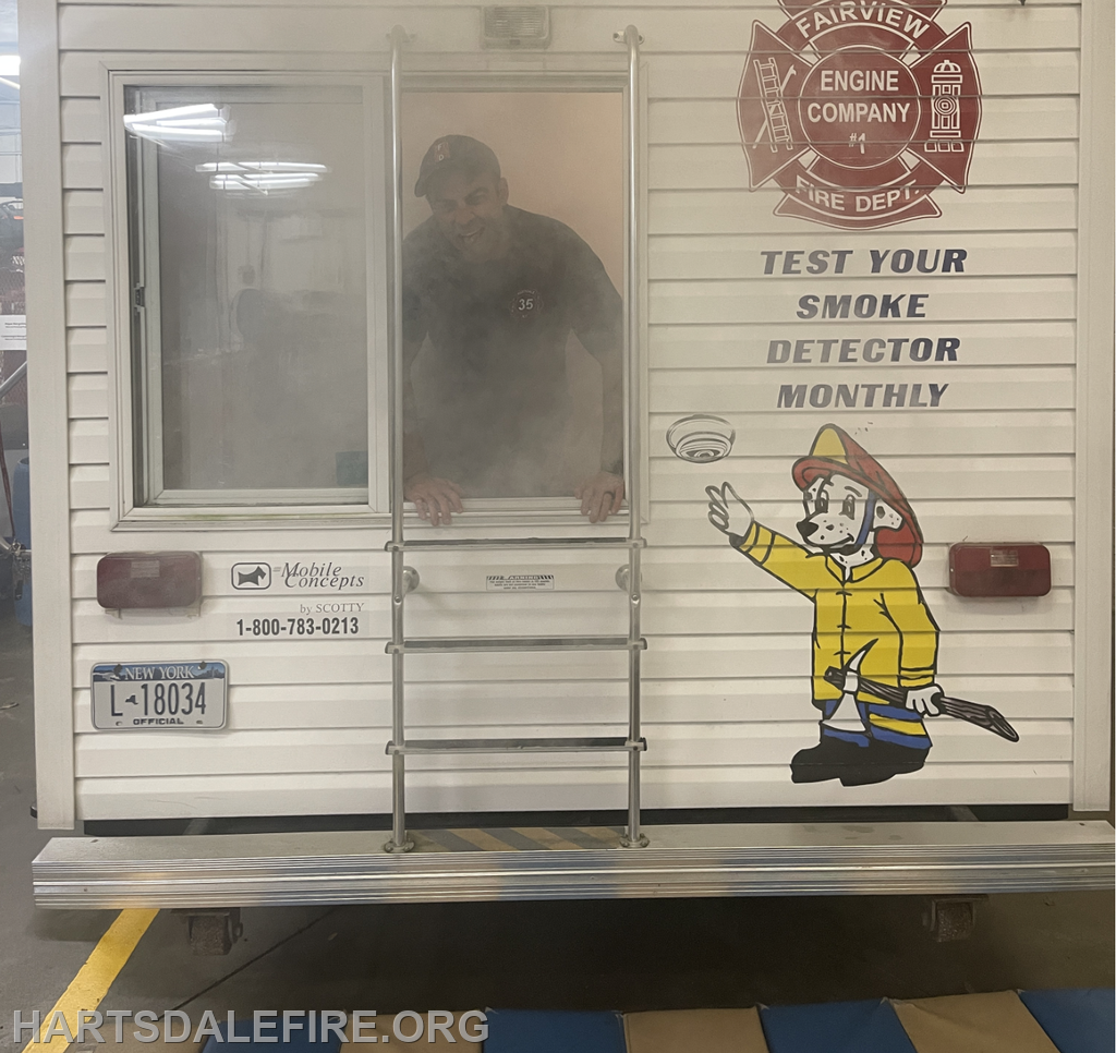 A firefighter interacts with a smoke-filled training mobile unit, promoting smoke detector safety and testing.