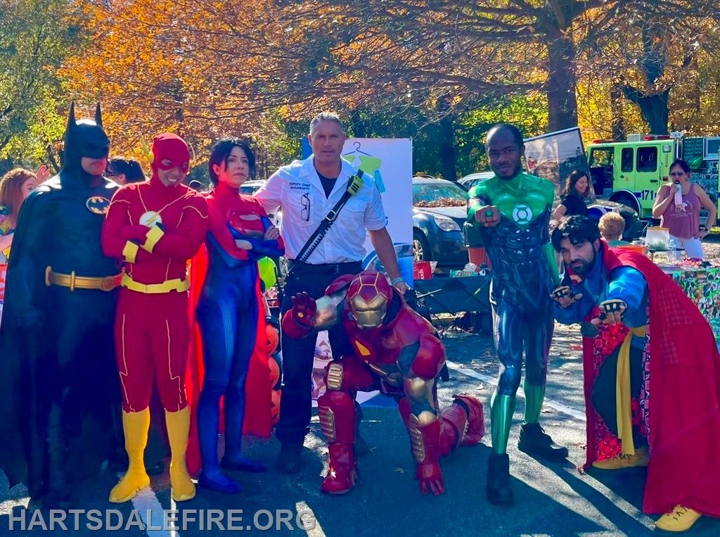 A group of people in superhero costumes, including Batman, Flash, and Iron Man, posing outdoors at an event.