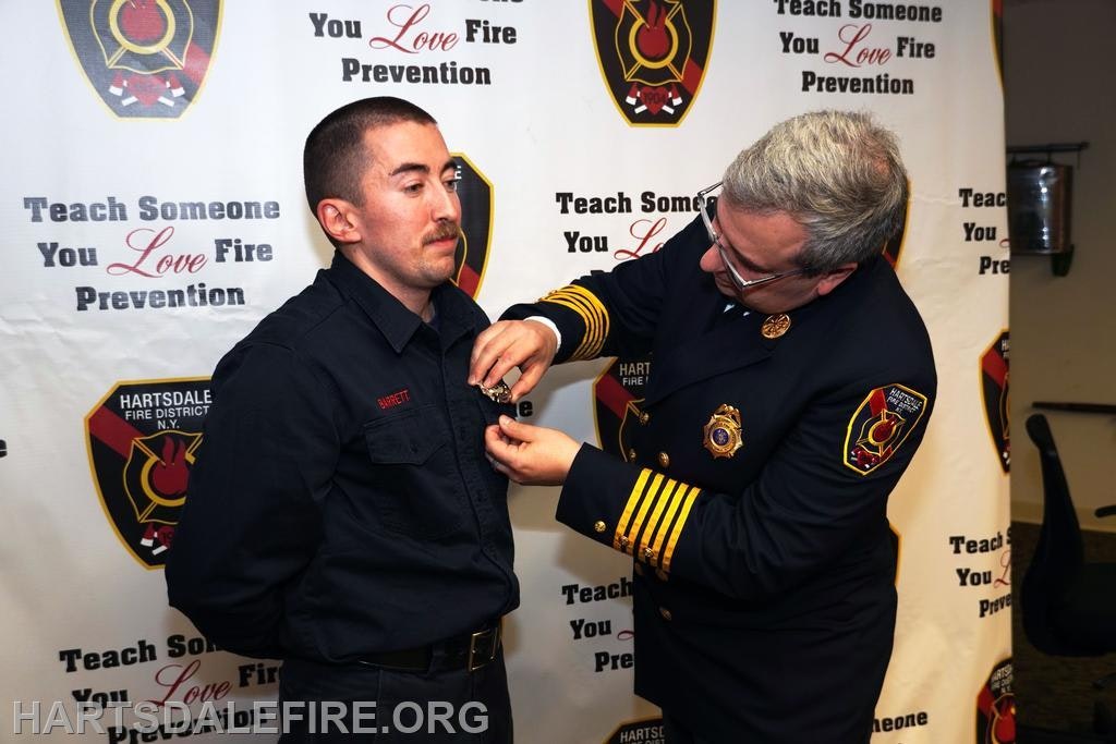 A man in a fire department uniform receives a badge from a chief officer at a fire prevention event.