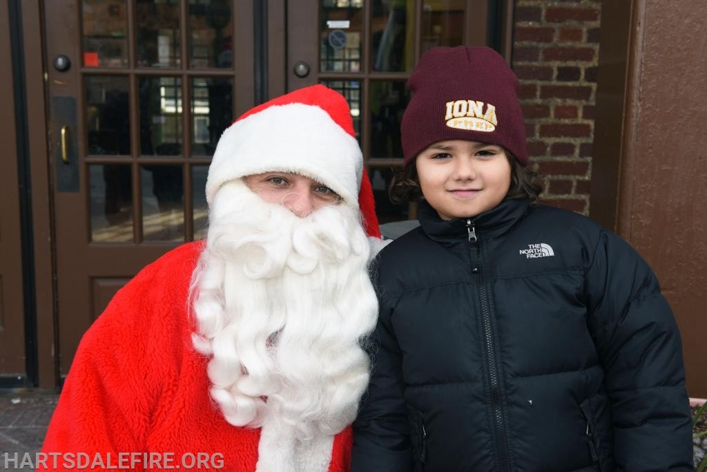 A person in a Santa outfit is posing with a child wearing a winter jacket and beanie.