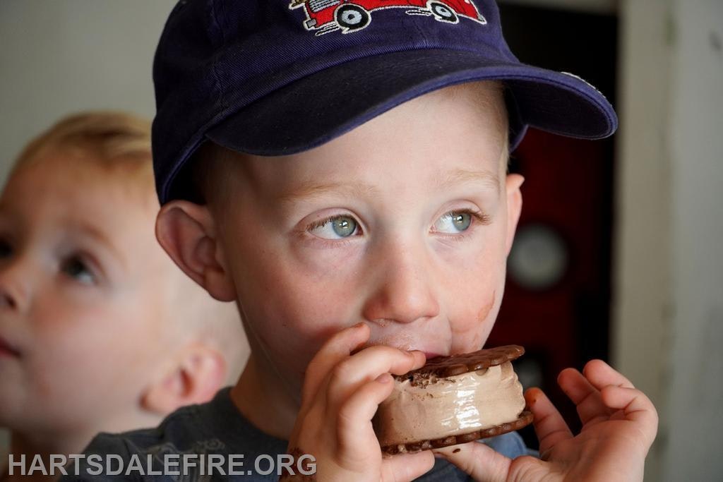 Two kids, one wearing a cap, enjoying an ice cream sandwich.