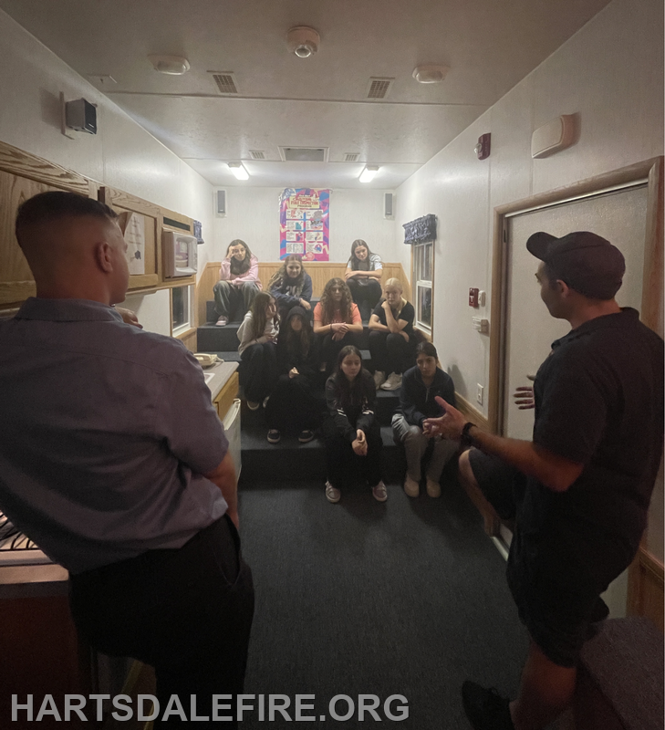 A group of young people sits in a room, listening attentively to two adults discussing something important.