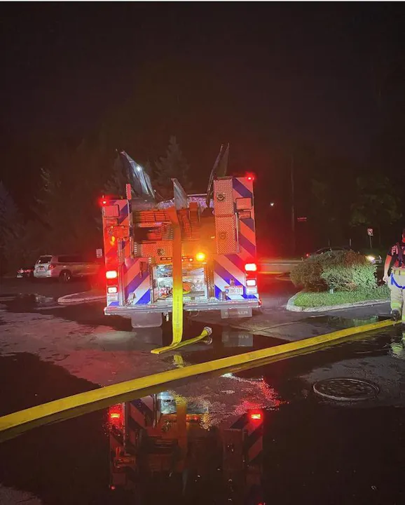 A fire truck at night with yellow hoses and reflections in puddles, indicating an emergency response scene.