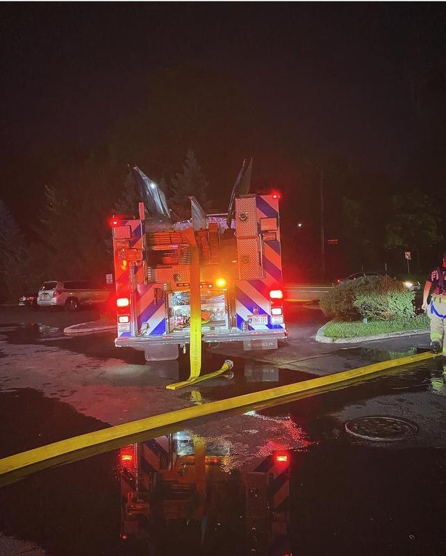 A fire truck at night with yellow hoses and reflections in puddles, indicating an emergency response scene.