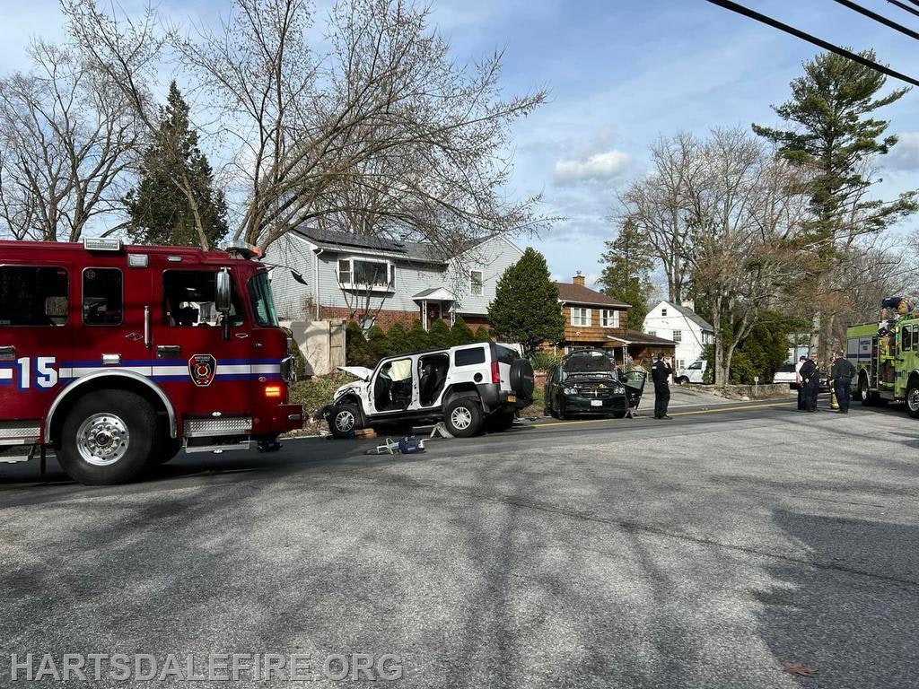 A fire truck and police officers are at the scene of an accident involving a damaged vehicle on a residential street.