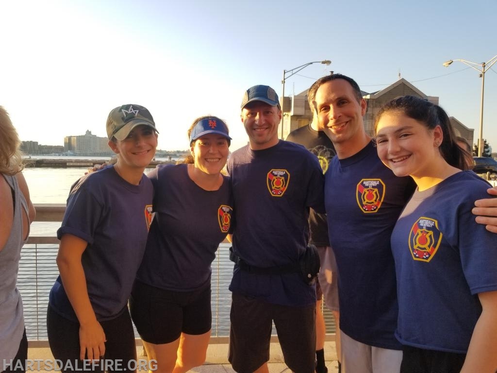 A group of people wearing matching fire department shirts, posing by a body of water at sunset.