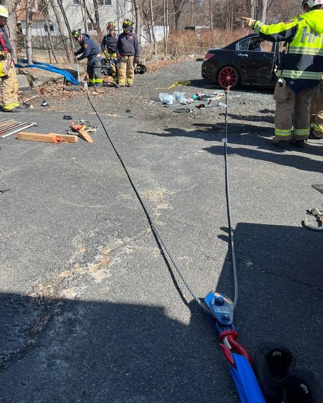 Firefighters are at an incident scene, using ropes and equipment, while some members work on the ground nearby.