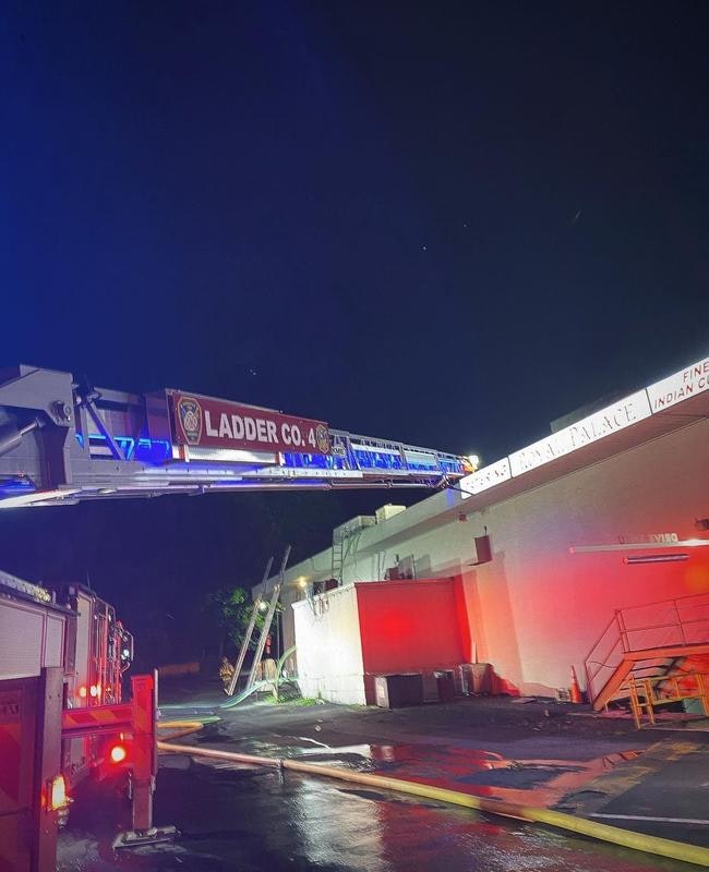 A fire truck ladder extends toward a building at night, with lights illuminating the scene, indicating a possible emergency situation.