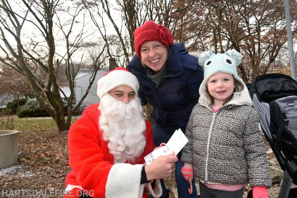 A person dressed as Santa Claus, a woman, and a child in winter attire pose outdoors.