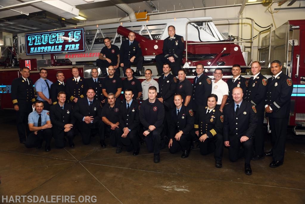 A group of firefighters posing in front of a fire truck labeled "Truck 15 Hartsdale Fire."