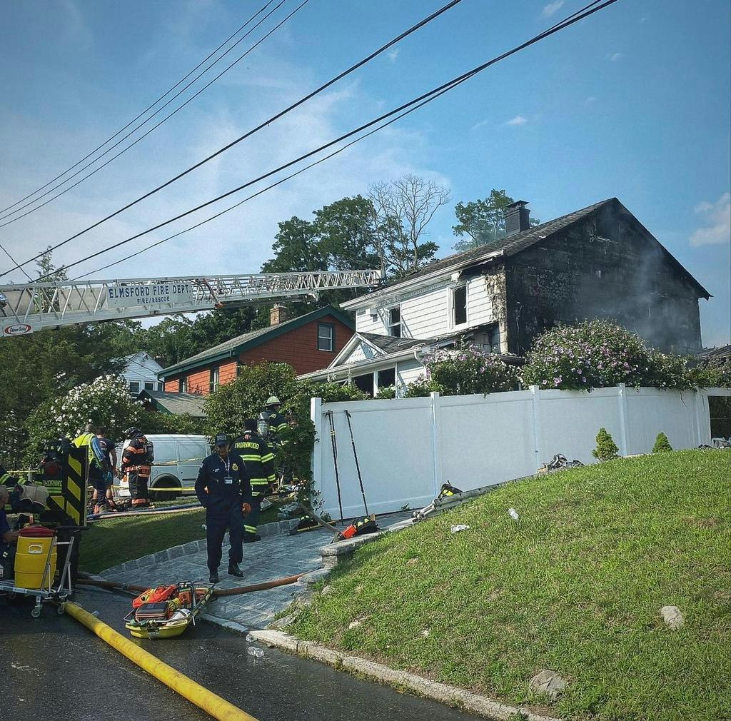 A fire truck from Elmsford Fire Department responds to a residential fire with visible damage on the upper floor.