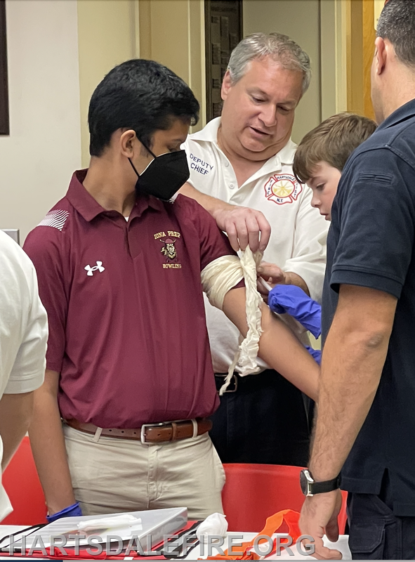 A group of people are practicing first aid, wrapping a bandage on someone's arm.