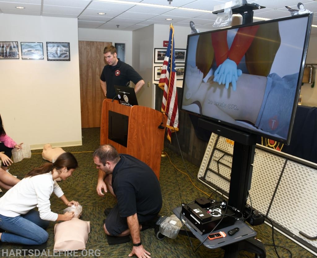 People practicing CPR on mannequins, with instructional video playing.
