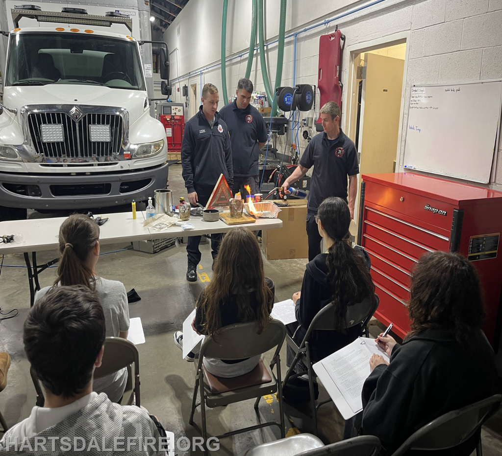 Firefighters demonstrate safety techniques to an audience, showcasing experiments and discussing fire prevention.