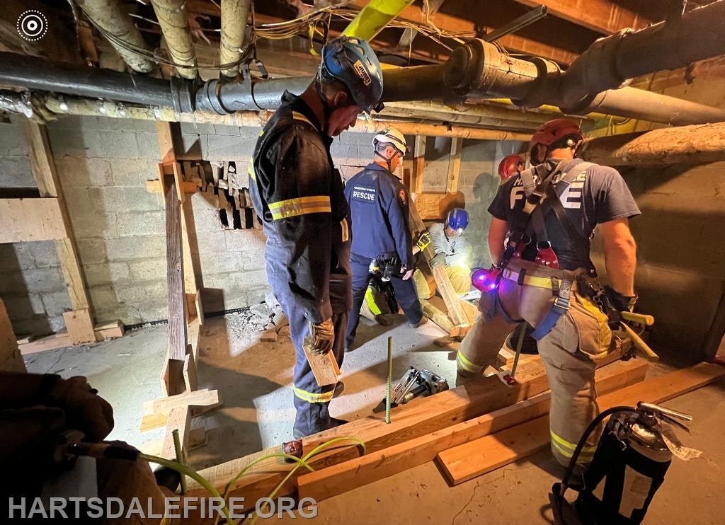 Firefighters performing a rescue operation in a basement with wooden support structures.