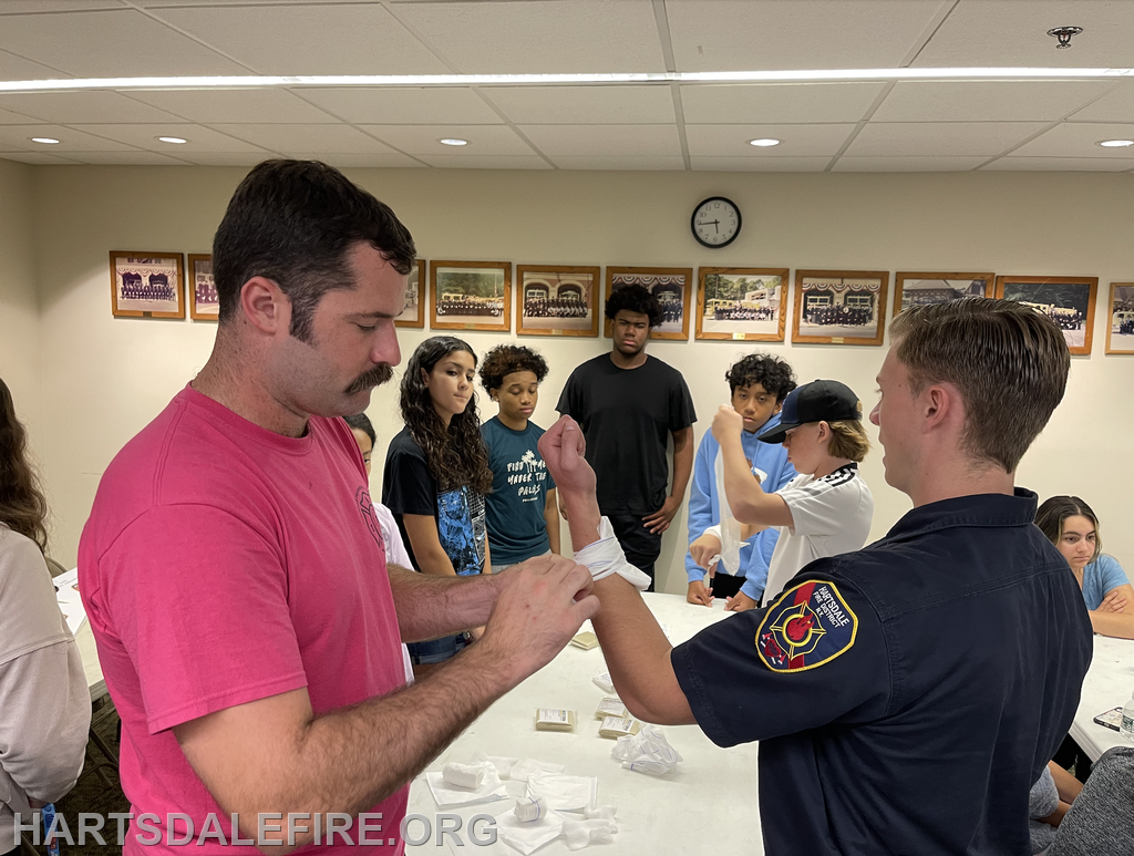 A group of people learning first aid, with a firefighter demonstrating bandaging techniques.