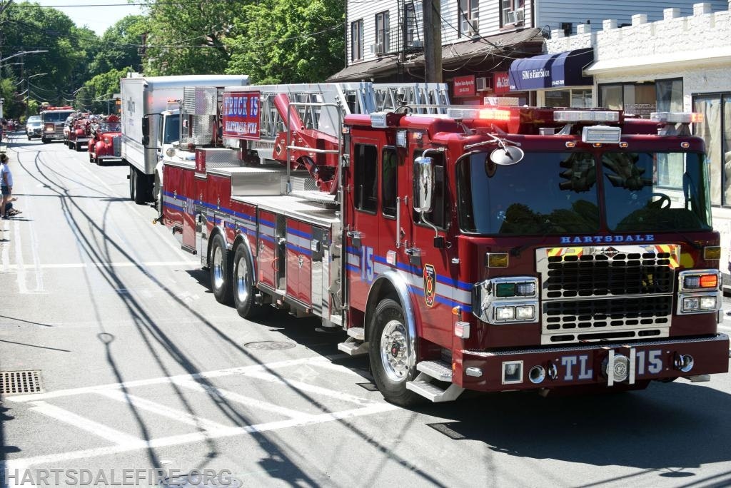 Red fire truck in a street parade with buildings and trees in the background.
