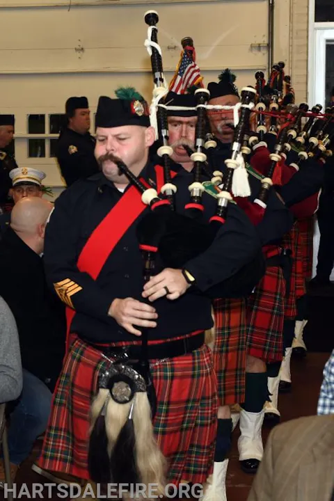 A group of people in kilts playing bagpipes inside a building.