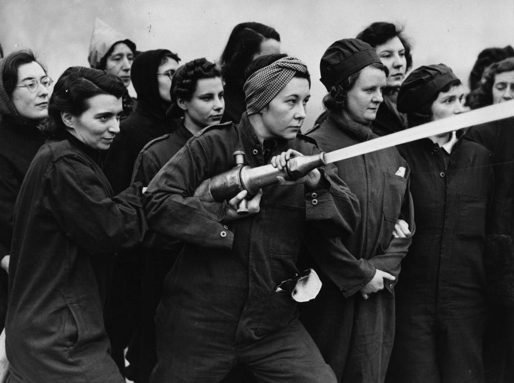 Women learning to use a fire hose, wearing work clothes, in a black and white photo.