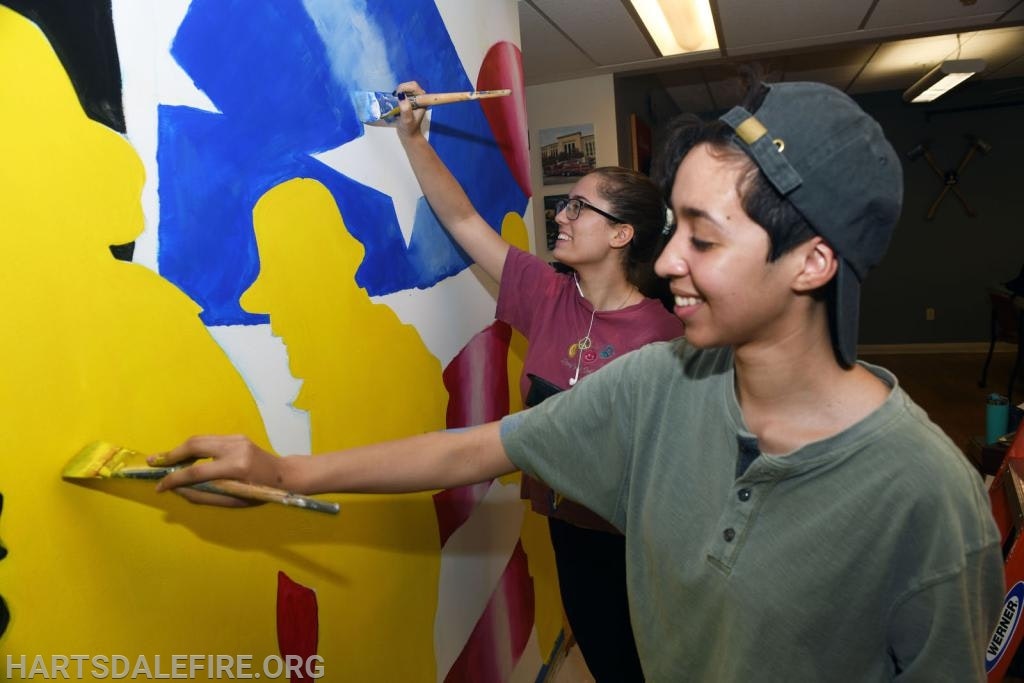 Two people painting a colorful mural with abstract shapes.