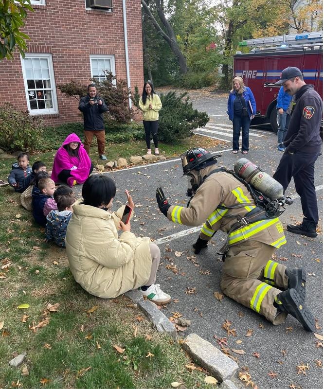 A firefighter interacts with a group of children and adults, creating a friendly atmosphere, possibly for a community event.