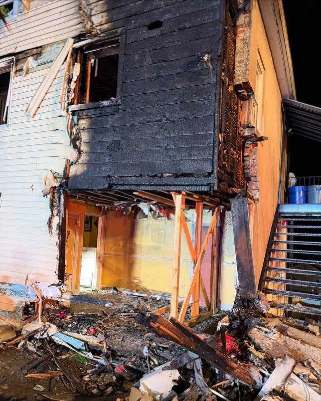 The image shows a damaged building with a charred exterior and debris, indicating recent fire damage.