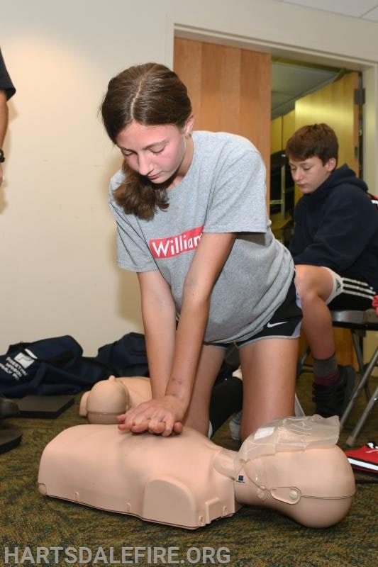 A girl practicing CPR on a dummy in a classroom setting.