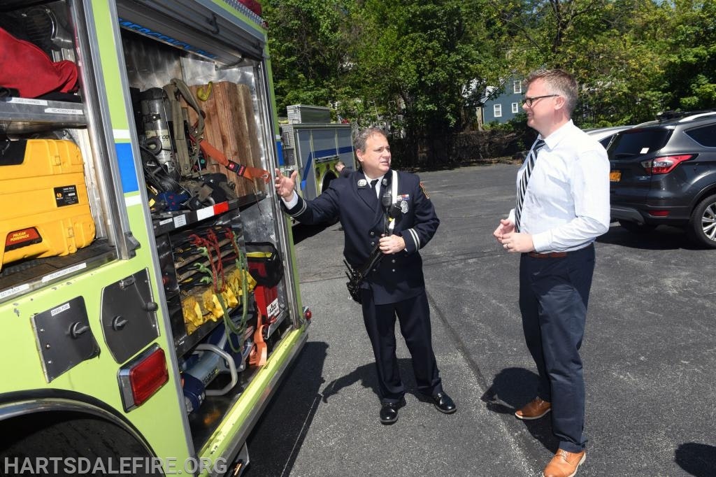 Two people talking near an open fire truck with rescue equipment.