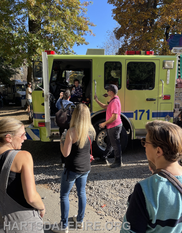 A yellow fire truck with people interacting, including a child inside. It’s likely a community event or demonstration.