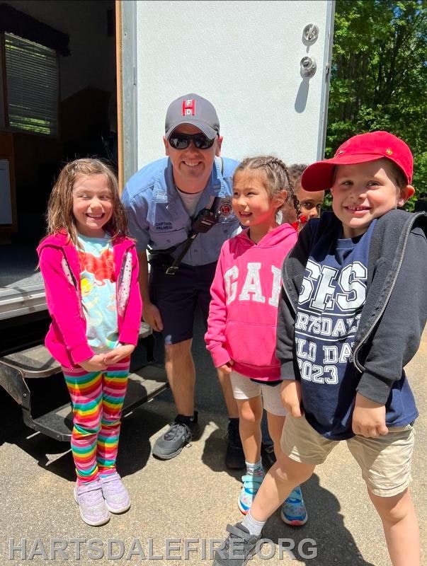 A group of children and an adult in uniform posing and smiling outdoors.