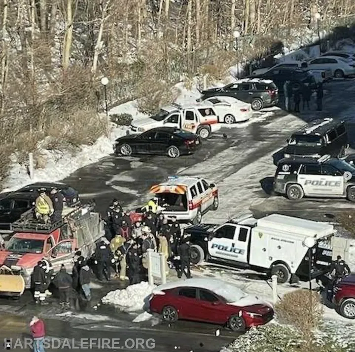 Emergency responders and police are gathered in a snowy area with multiple vehicles, likely responding to an incident.