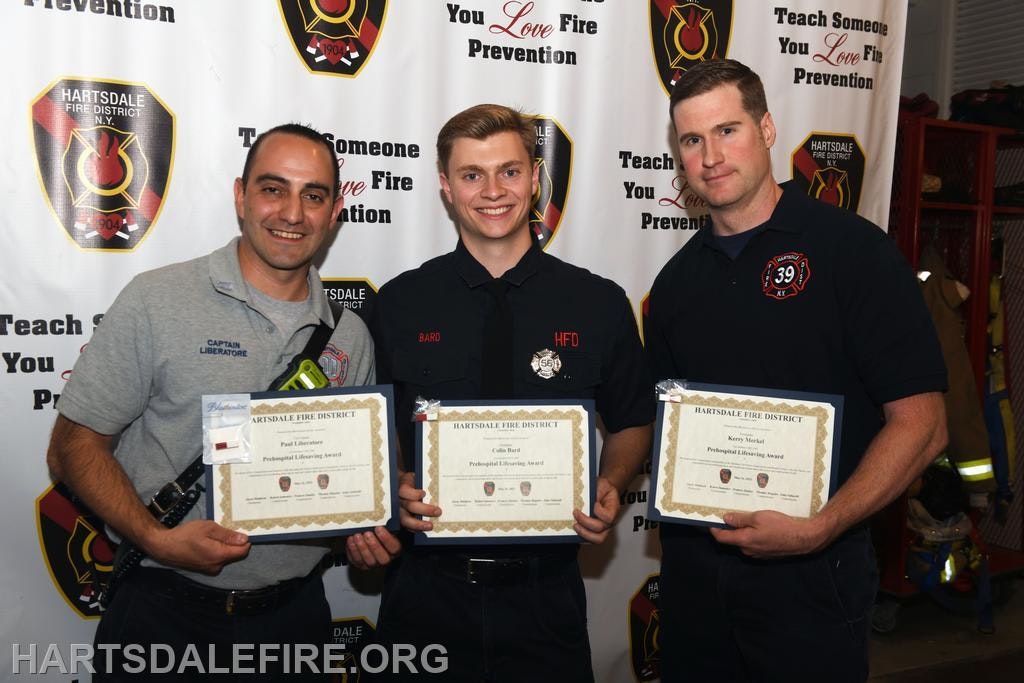 Three men holding certificates in front of a fire prevention banner.