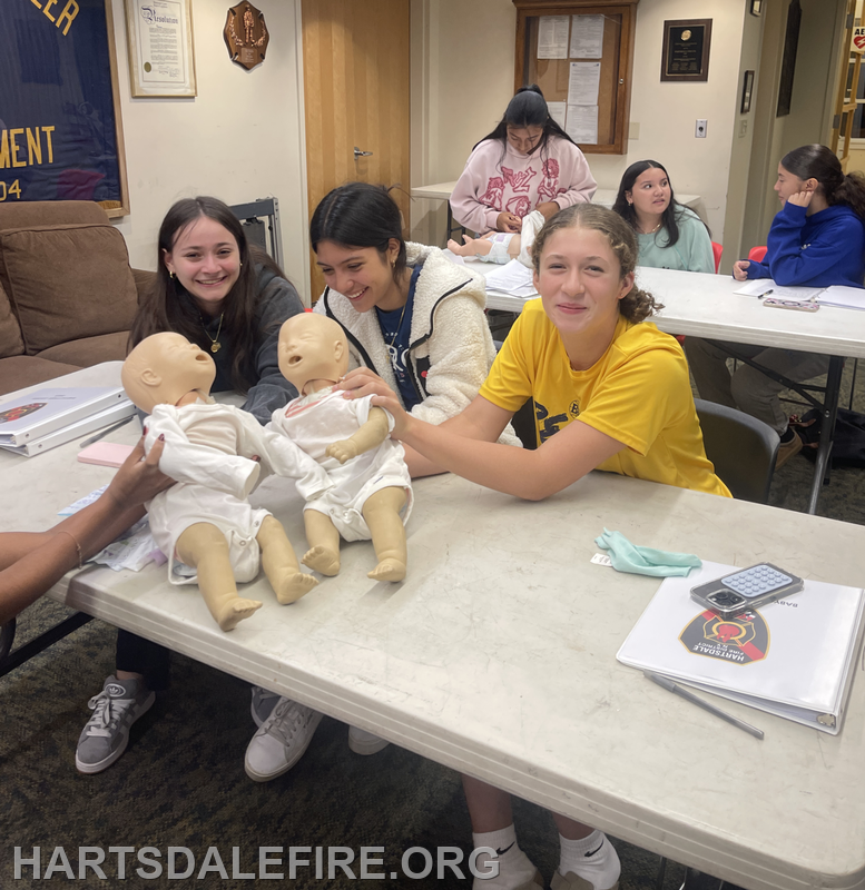 A group of young women is practicing with baby dolls, likely in a learning environment focused on caregiving or first aid.