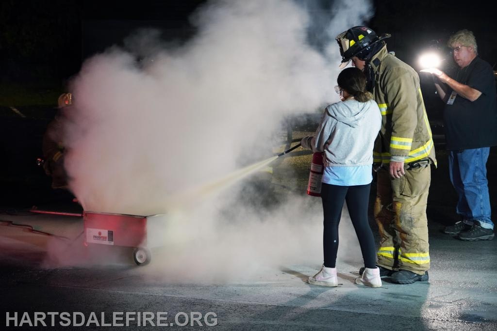 Firefighter assisting a person using a fire extinguisher, creating a cloud of smoke.