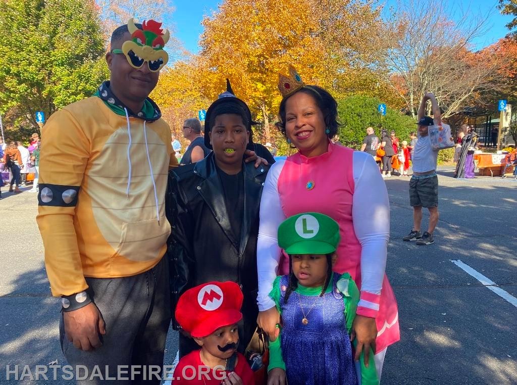 A family dressed in Super Mario-themed costumes posing outdoors, with vibrant fall foliage in the background.
