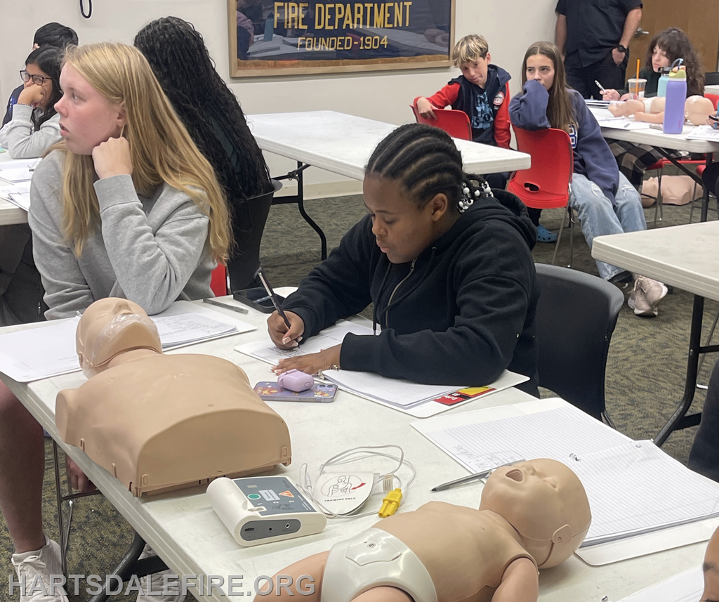 A classroom scene with students learning, notebooks on tables, and CPR mannequins in front of them.