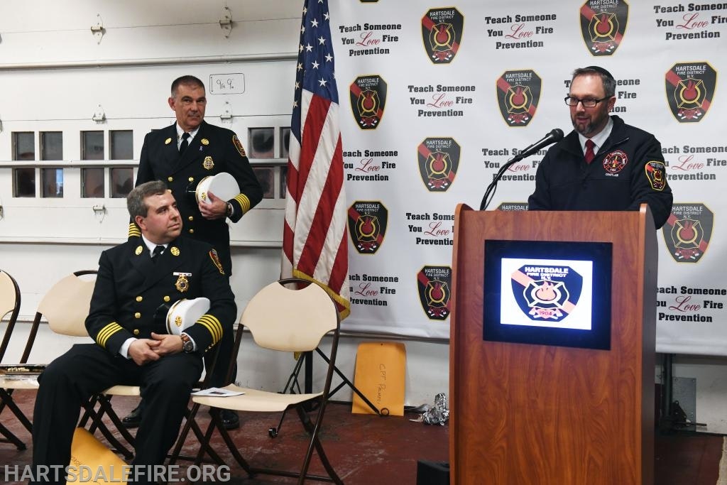 Three fire officials in uniform at a podium with Hartsdale Fire Department logos and an American flag.
